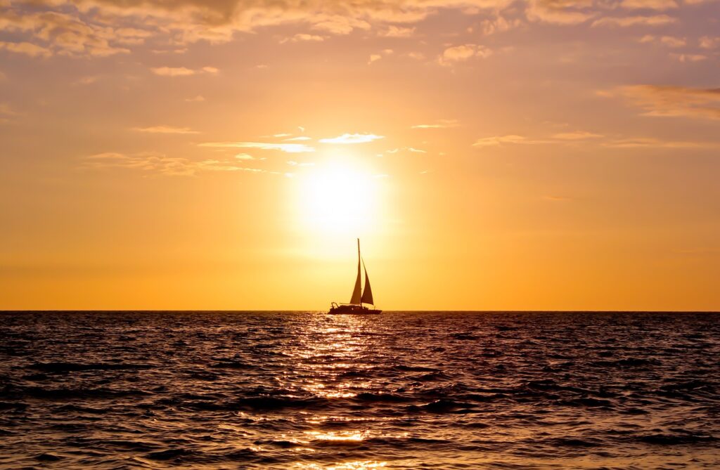 Boat at sail in the sea with a large sun shining on it