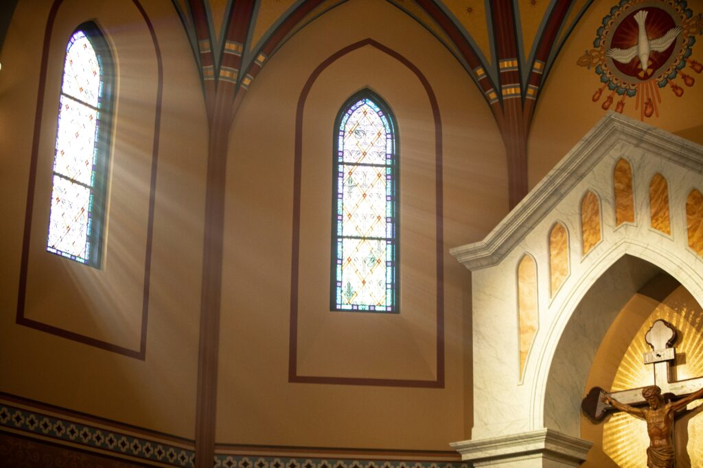 Sunlight shining through church stained glass windows on the crucified Christ with the symbol of the Holy Spirit above Him in the sanctuary of the church