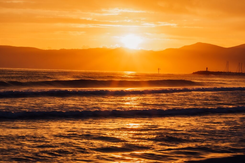 Sun shining over the ocean with waves at the shore