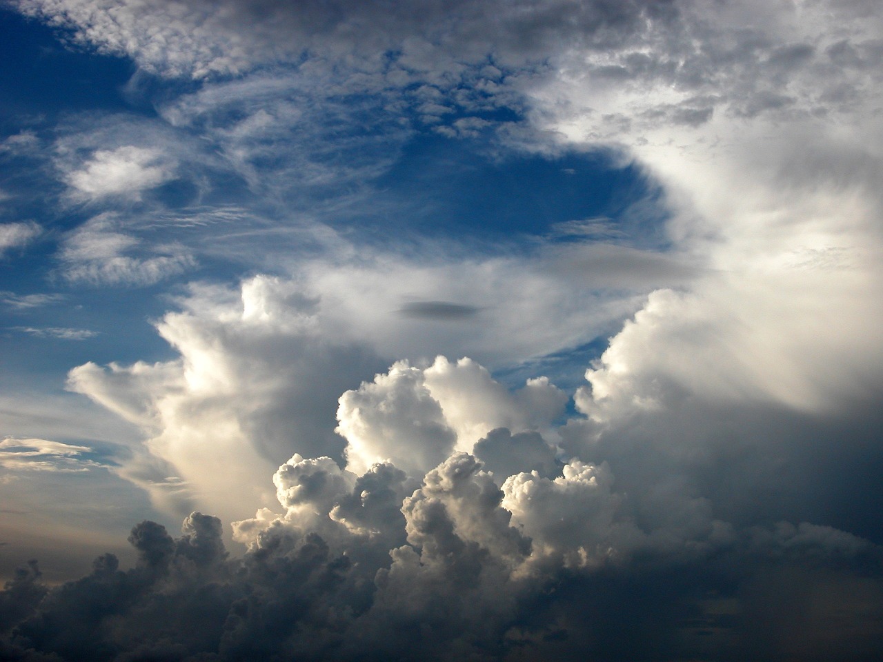 Several formations of clouds in the sky with sunlight shining on the higher clouds and blue sky