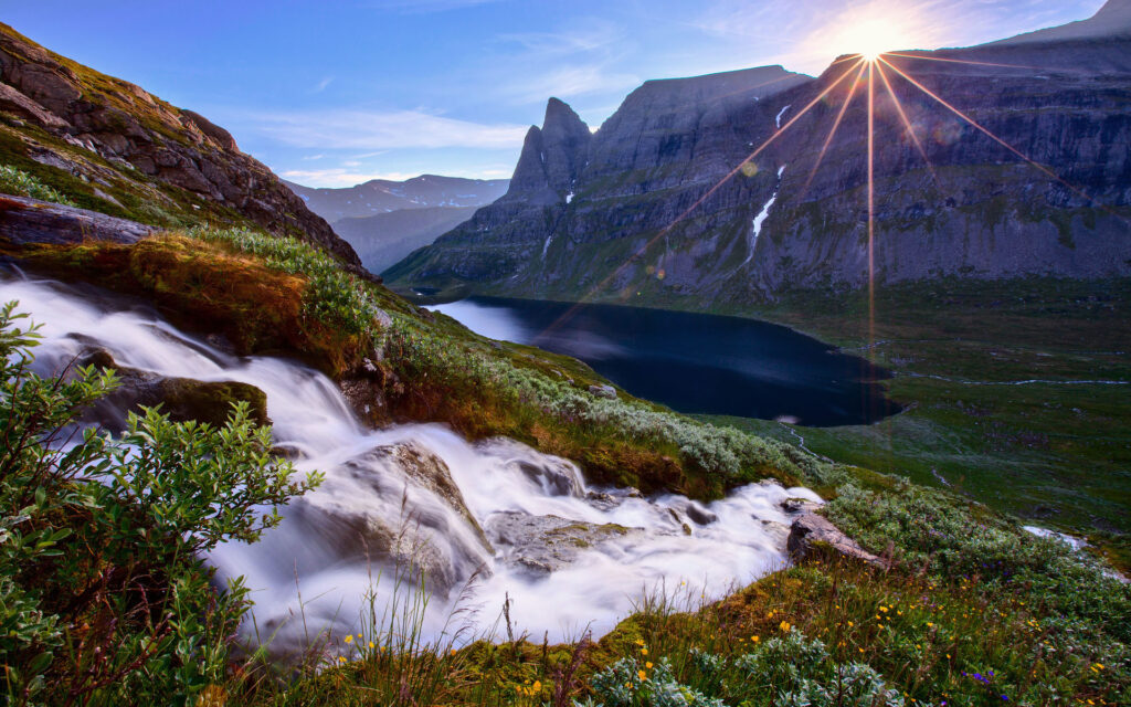 Clean spring water rushing down the side of a mountain with the rays of the sun shining in the distance